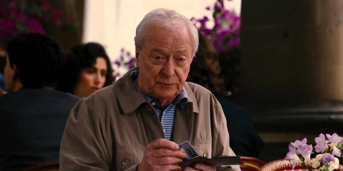 An old man sitting at a table putting away his credit card.