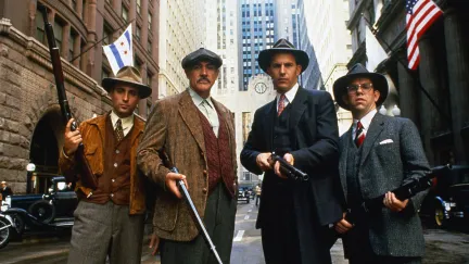 A group of four well dressed man carry shotguns in the street in 