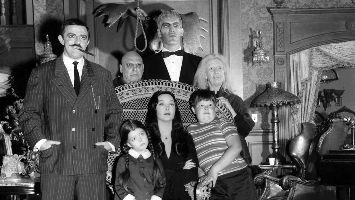 The cast of the Addams Family sits in a gothic living room in The Addams Family