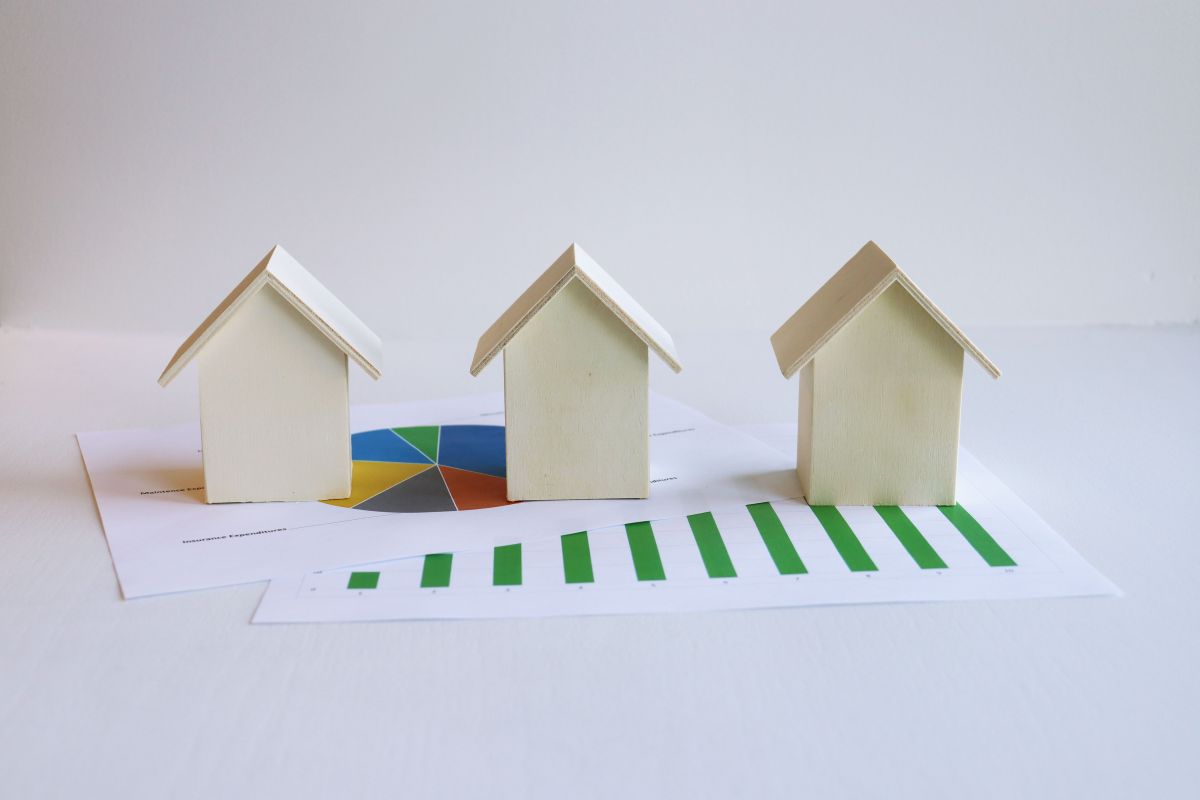 Three small model houses sit on top of pieces of paper showing graphs.