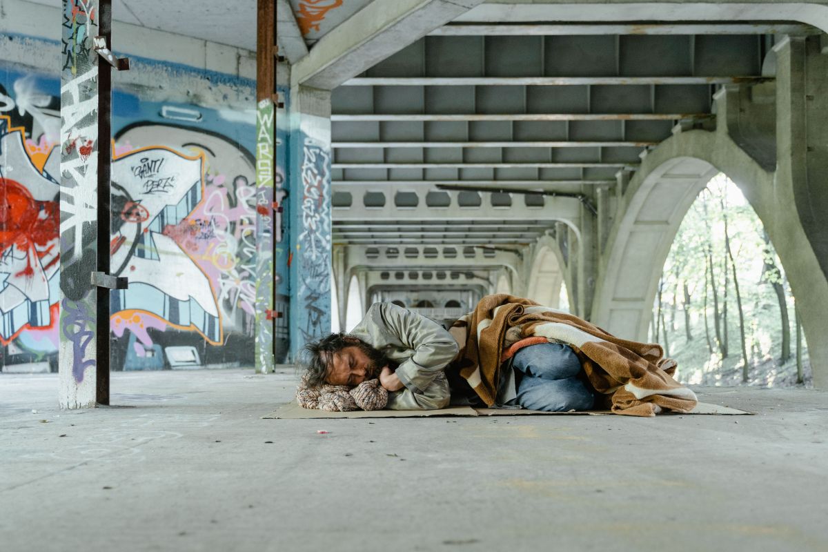 A homeless man sleeps under a bridge with graffiti on the walls.