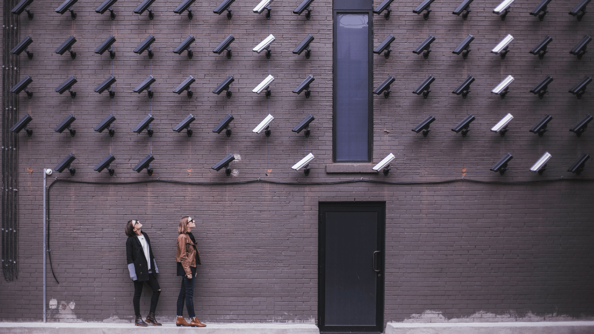 Many cameras on a brick wall pointing down at two people