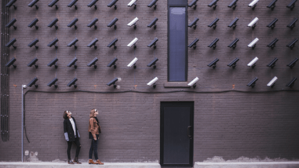 Many cameras on a brick wall pointing down at two people