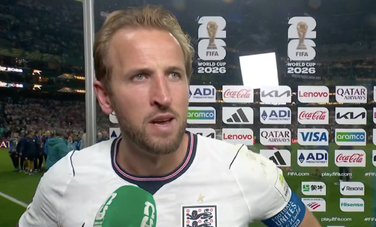 Man by a board at a football match being interviewed