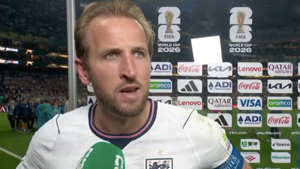 Man by a board at a football match being interviewed