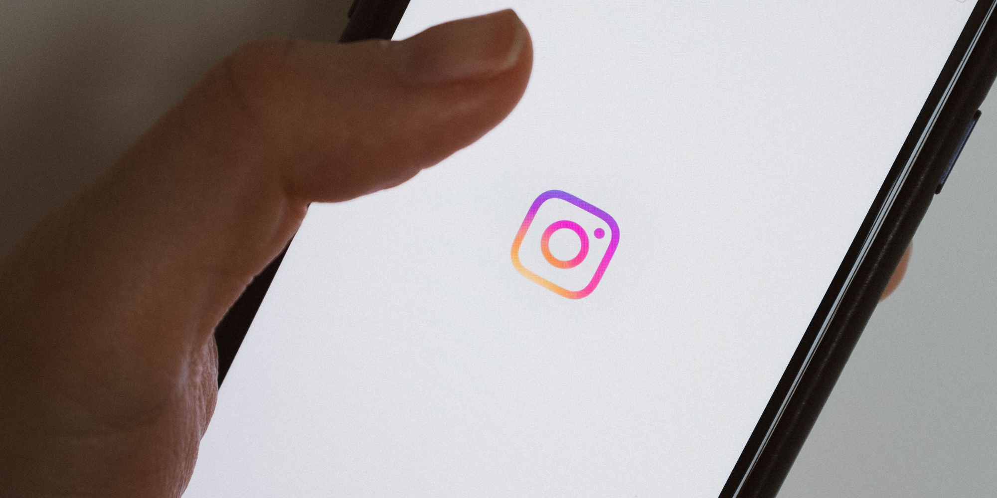 An up-close image of a hand holding a phone. The phone has the Instagram logo on it.