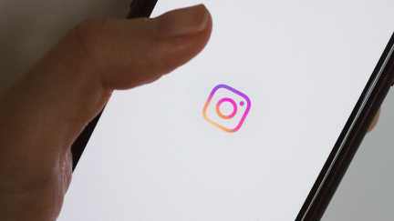 An up-close image of a hand holding a phone. The phone has the Instagram logo on it.