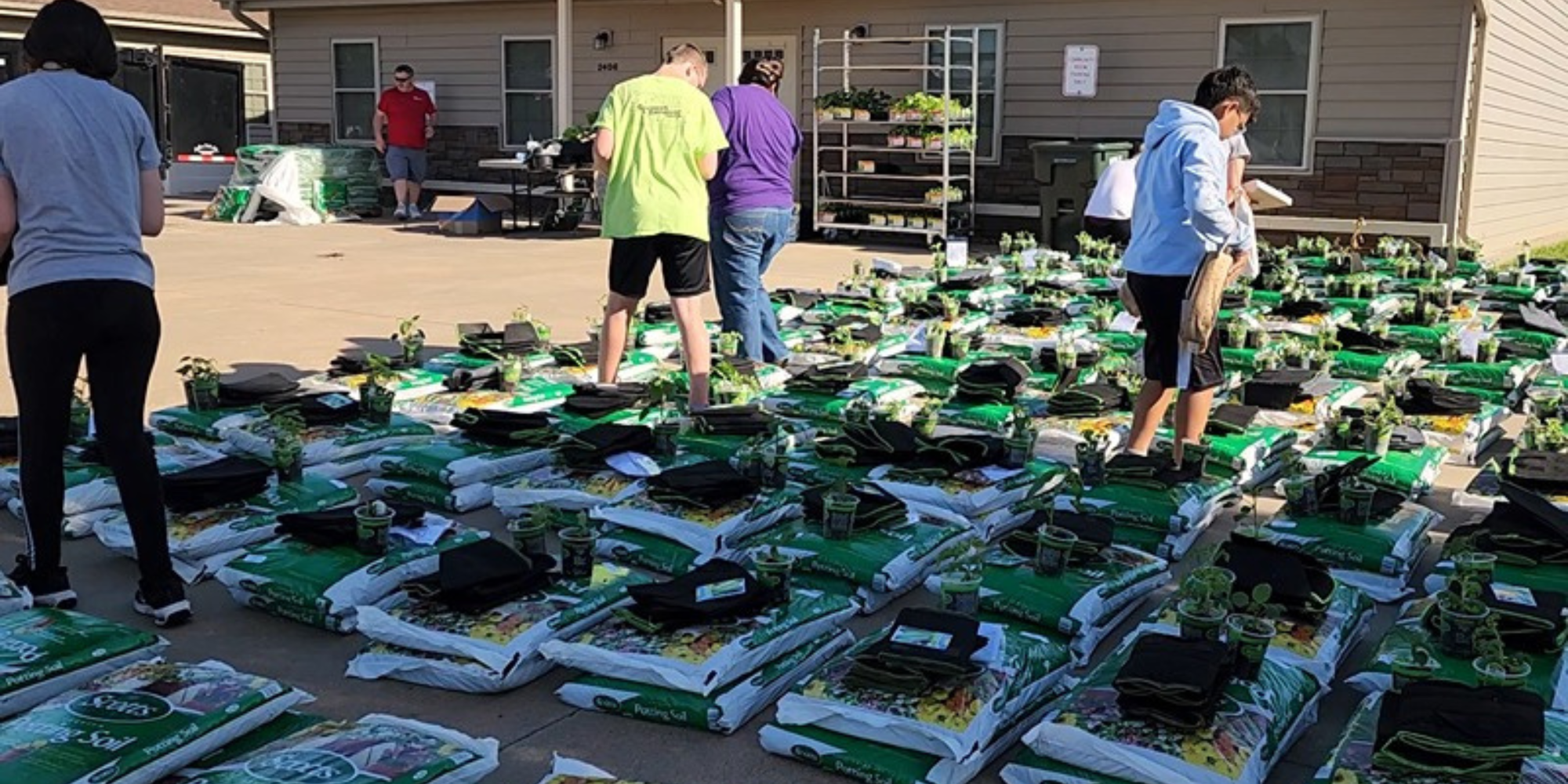 People standing around container gardens and potting soil