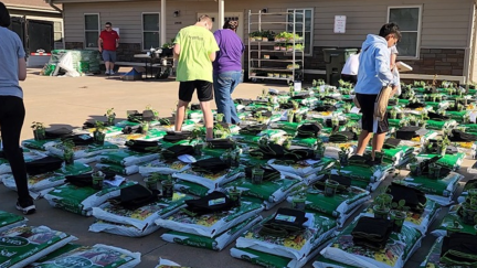People standing around container gardens and potting soil