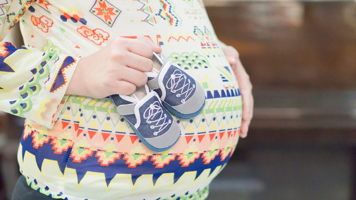A pregnant belly and a hand holding baby shoes