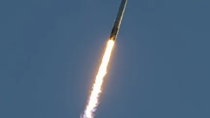 A SpaceX Falcon 9 launches into space with fire trailing it.